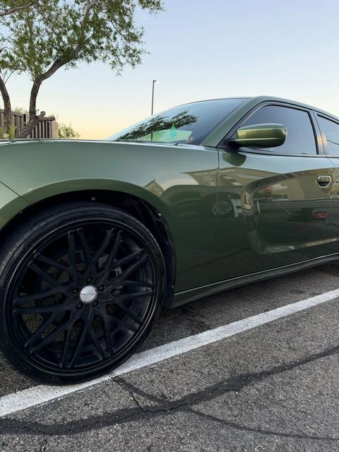 Olive-green Dodge Charger with black multi-spoke wheel, side view in a parking space at sunset
