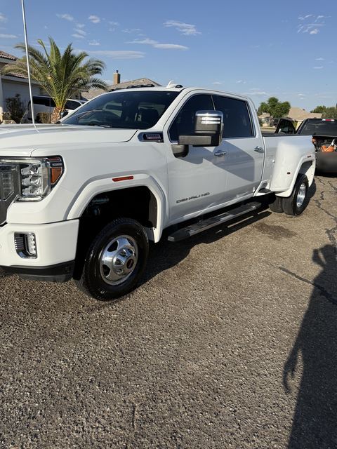 White GMC Sierra Denali HD dually pickup, side view on a gravel driveway