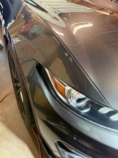 Close-up of a dark gray car's front fender and headlight in a garage after detailing (labeled 'After')